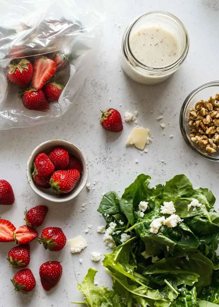 Ingredients for strawberry salad recipe including fresh strawberries and greens