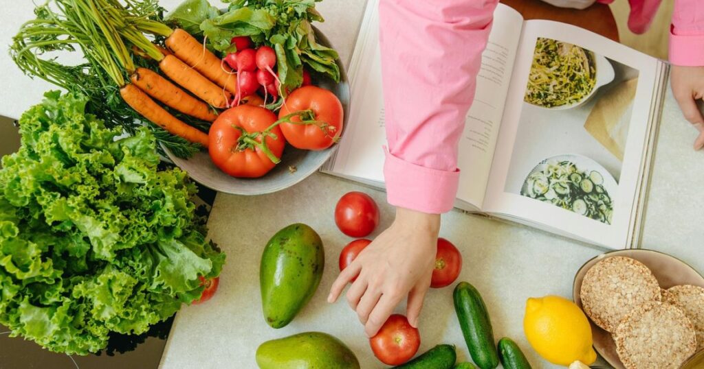 This bright and colorful image captures the essence of seasonal cooking, perfect for an article titled "40 Fresh Healthy Spring Recipes to Try Now." With leafy greens, ripe tomatoes, avocados, carrots, radishes, and a cookbook open to spring salad ideas, it reflects a wholesome approach to springtime meals. Ideal for health-conscious food lovers, this image sets the tone for nutritious recipes packed with freshness and flavor.