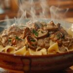 Steaming bowl of ground beef stroganoff with mushrooms and creamy sauce served over wide egg noodles.