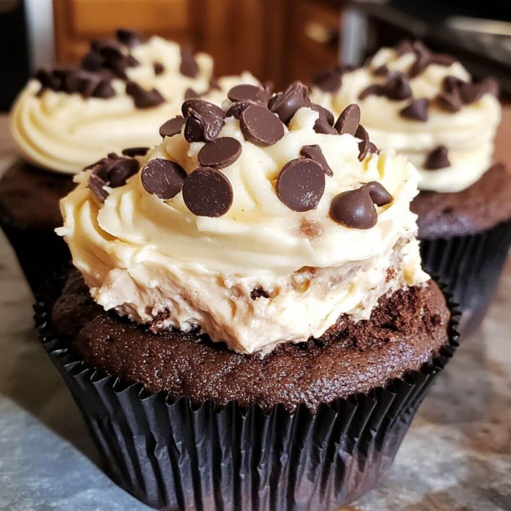 Close-up of cheesecake-stuffed chocolate cupcakes topped with creamy frosting and chocolate chips.
