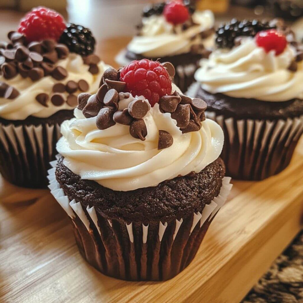 Chocolate cupcakes with cream cheese frosting, chocolate chips, and fresh berries served on a wooden board.