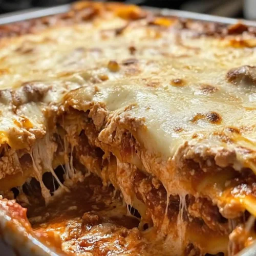 Dumpling lasagna with melted cheese, cut open to show layered noodles, meat sauce, and stretchy mozzarella inside a baking dish.